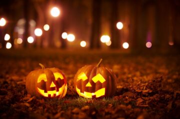 Two jack-o'-lanterns are in dark forest with orange lights.