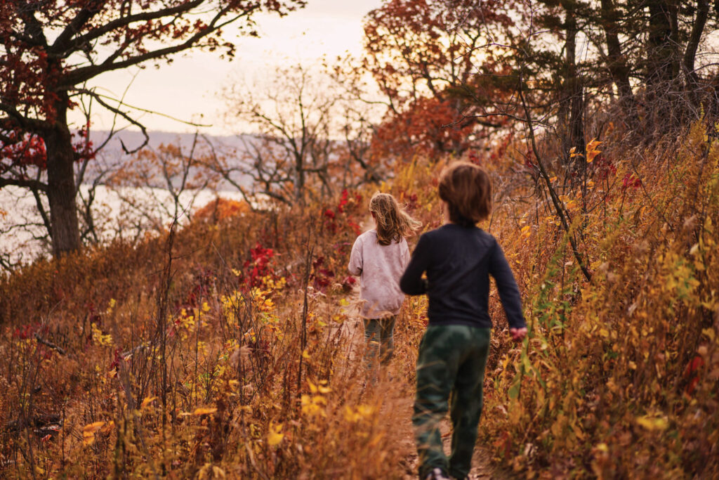 Two children run down a trail in the fall woods that overlooks the Mississippi River.