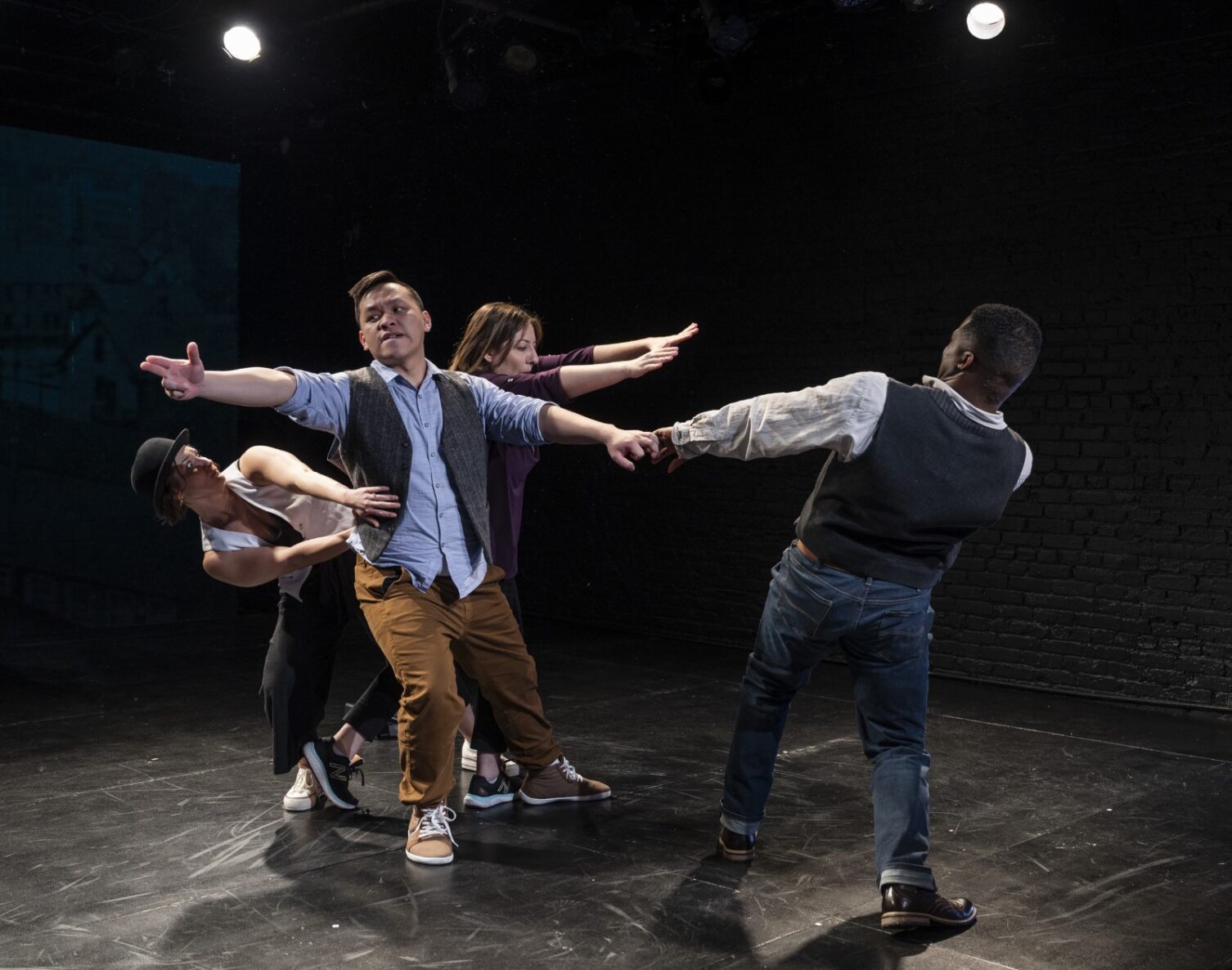 Four actors on stage are twisted in a slow motion gun scene
