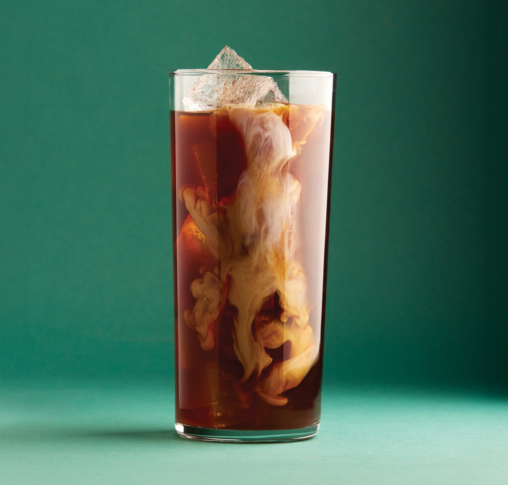 A portrait of an iced coffee with cream swirling through it on a green background