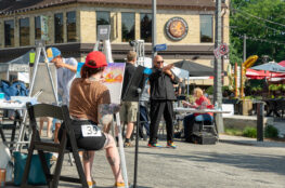 A person is sitting in a chair and painting on a canvas that is propped up on an easel.