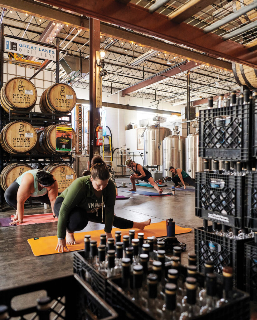 People practicing yoga at Great Lakes Distillery surrounded by barrels and distillery equipment, organized by MKE Yoga Social.