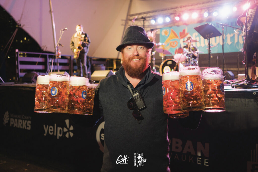 A red head bearded man holds eight steins of beer at the Octoberfest Celebration at Cathedral Square Park in Milwaukee, WI