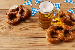 Beer Fest concept with pretzel, mug of beer and blue simbol flag on wood background, copy space, top view, flat lay
