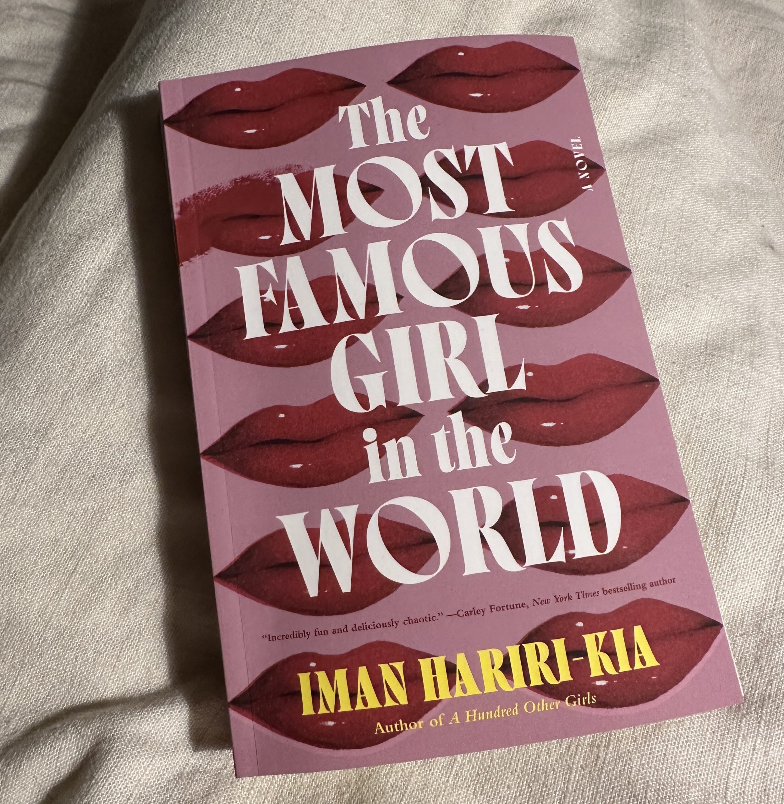 'The Most Famous Girl in the World' by Iman Hariri-Kia. A pink book with red lips all over it sitting on a white blanket.
