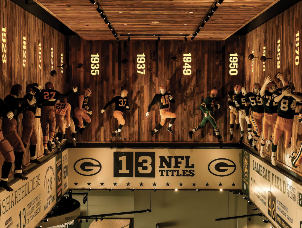 Green Bay Packers Hall of Fame exhibit showcasing life-sized player mannequins, historical years, and team achievements displayed on wooden walls.