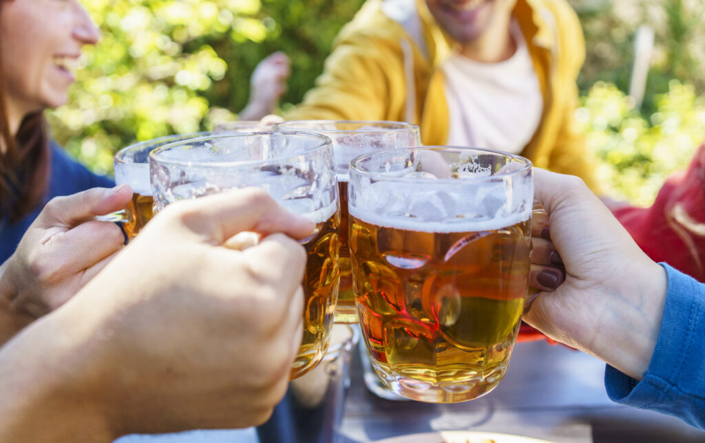 Young friends drinking and toasting beer pints at brewery bar garden out side - Beverage life style concept with guy and girls having fun together at happy hour