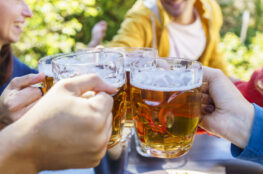 Young friends drinking and toasting beer pints at brewery bar garden out side - Beverage life style concept with guy and girls having fun together at happy hour
