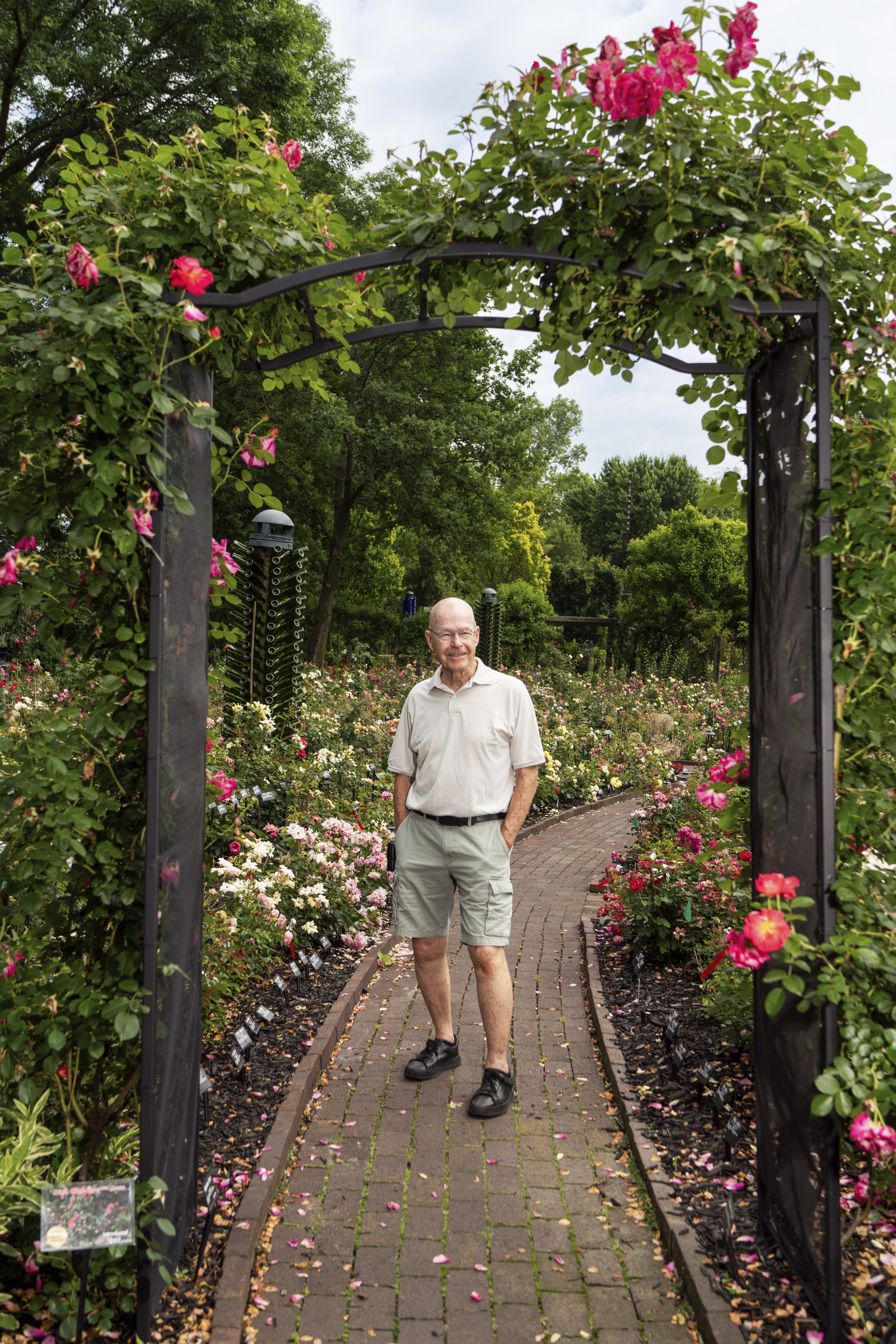 Will Radler stands at a arch adorned with roses in his botanical garden and rosarium.