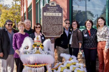 Commemoration ceremony for a historical marker on Martin Luther King Drive in Milwaukee, WI. The photo features a diverse group of people, the descendants and family members of Fred Moy, smiling as they stand next to the official dark brown and gold plaque.