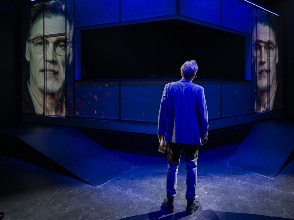 Actor Peter Bradbury stares at two images of his face on a screen during the Milwaukee Rep production of "McNeal."