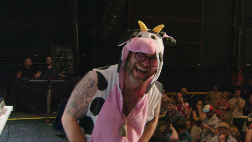 A man wearing a cow hoodie laughs in front of an audience.