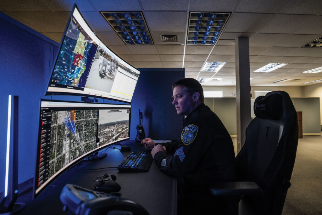 A police sergeant looks at two monitors of maps and drone footage of Milwaukee.