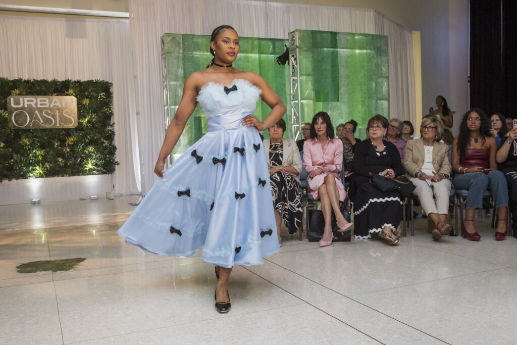 A model wearing a blue dress with several small black bows walks the runway at the Mount Mary Fashion Show.