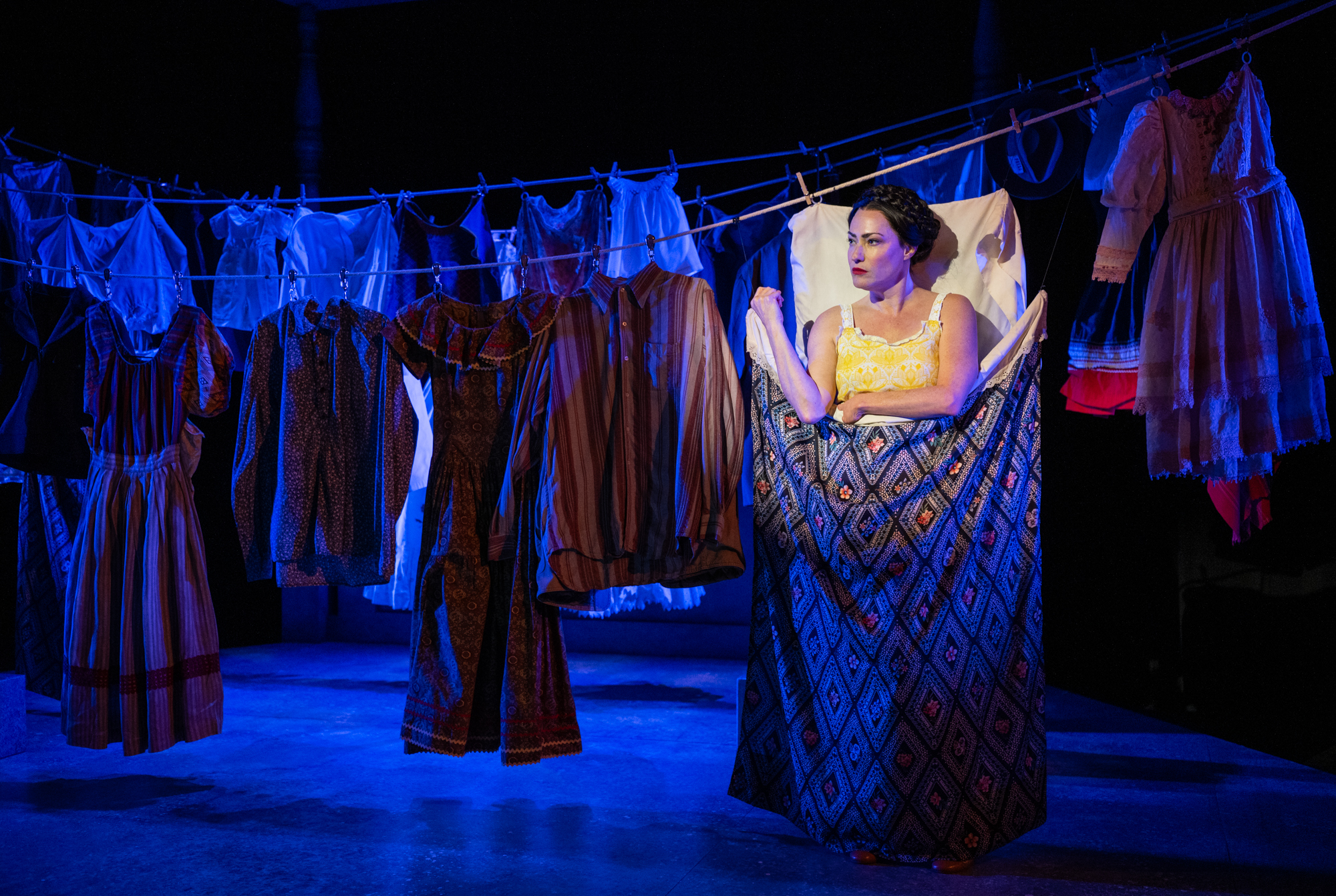 Vanessa Severo performing as Frida Kahlo, standing against clothes on a clothesline as if she's lying in bed, in Milwaukee Rep's "Frida...A Self Portrait."