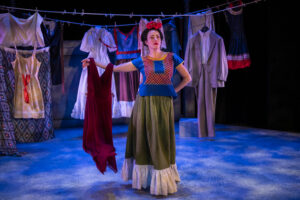 Vanessa Severo performing as Frida Kahlo, holding up a red dress as she pantomimes another character, in Milwaukee Rep's "Frida...A Self Portrait."