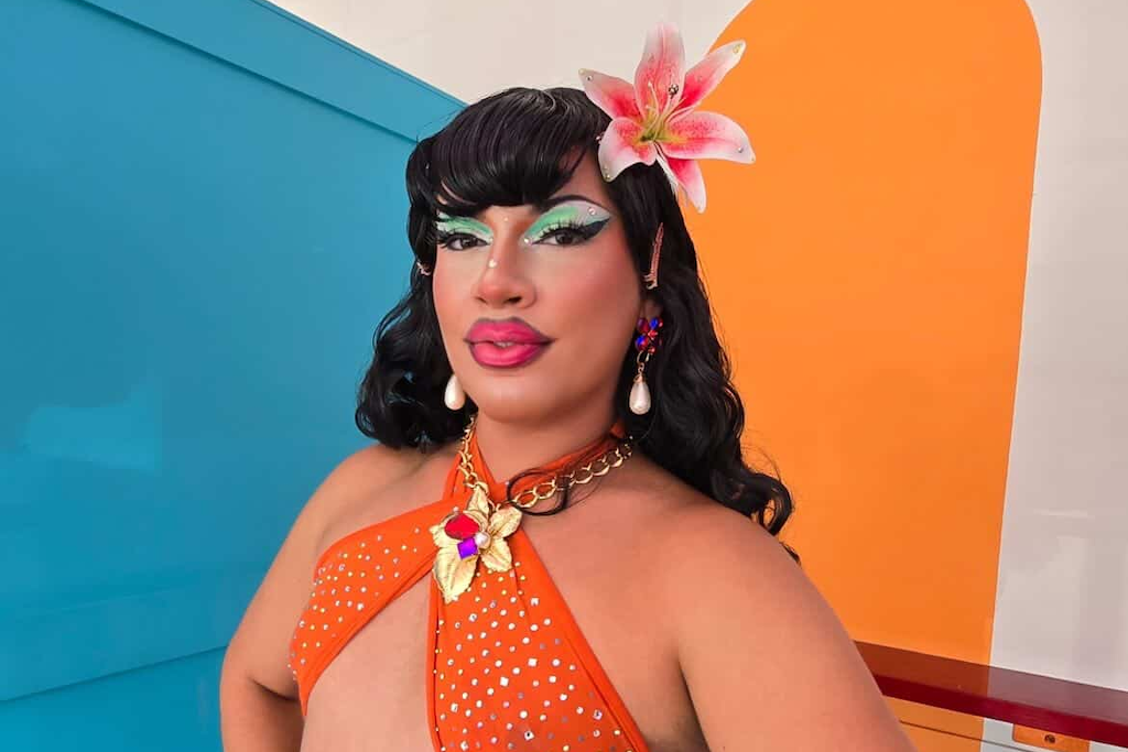 Milwaukee drag queen Susie Starlet posing with a flower in her hair and an orange dress.