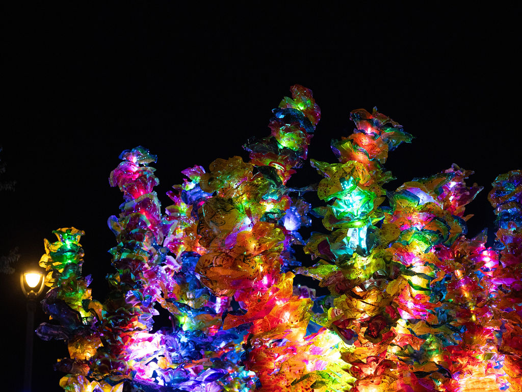 A brightly illuminated outdoor art installation made of colorful, translucent forms glows against the night sky.