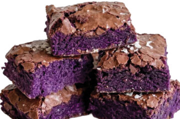 A stack of square ube brownies featuring vibrant purple centers and shiny crackled tops.