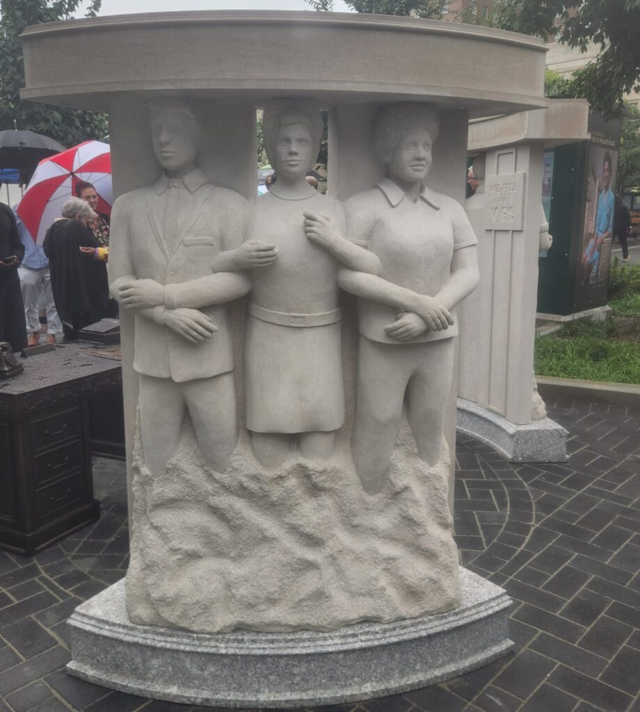 A marble looking sculpture of three people with arms linked.