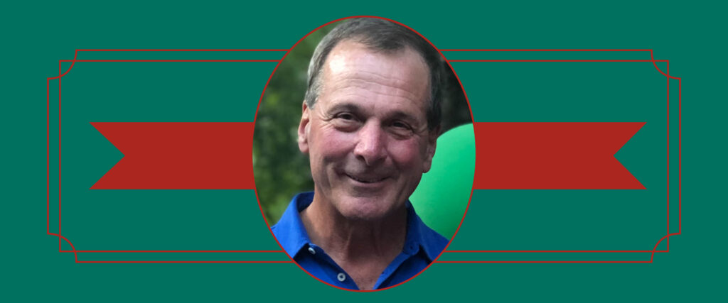 A graphic memorial-style portrait features a smiling man in a blue polo shirt centered inside an oval frame. The portrait sits against a deep green background with thin red decorative borders and a broad red ribbon-like banner extending horizontally behind it.